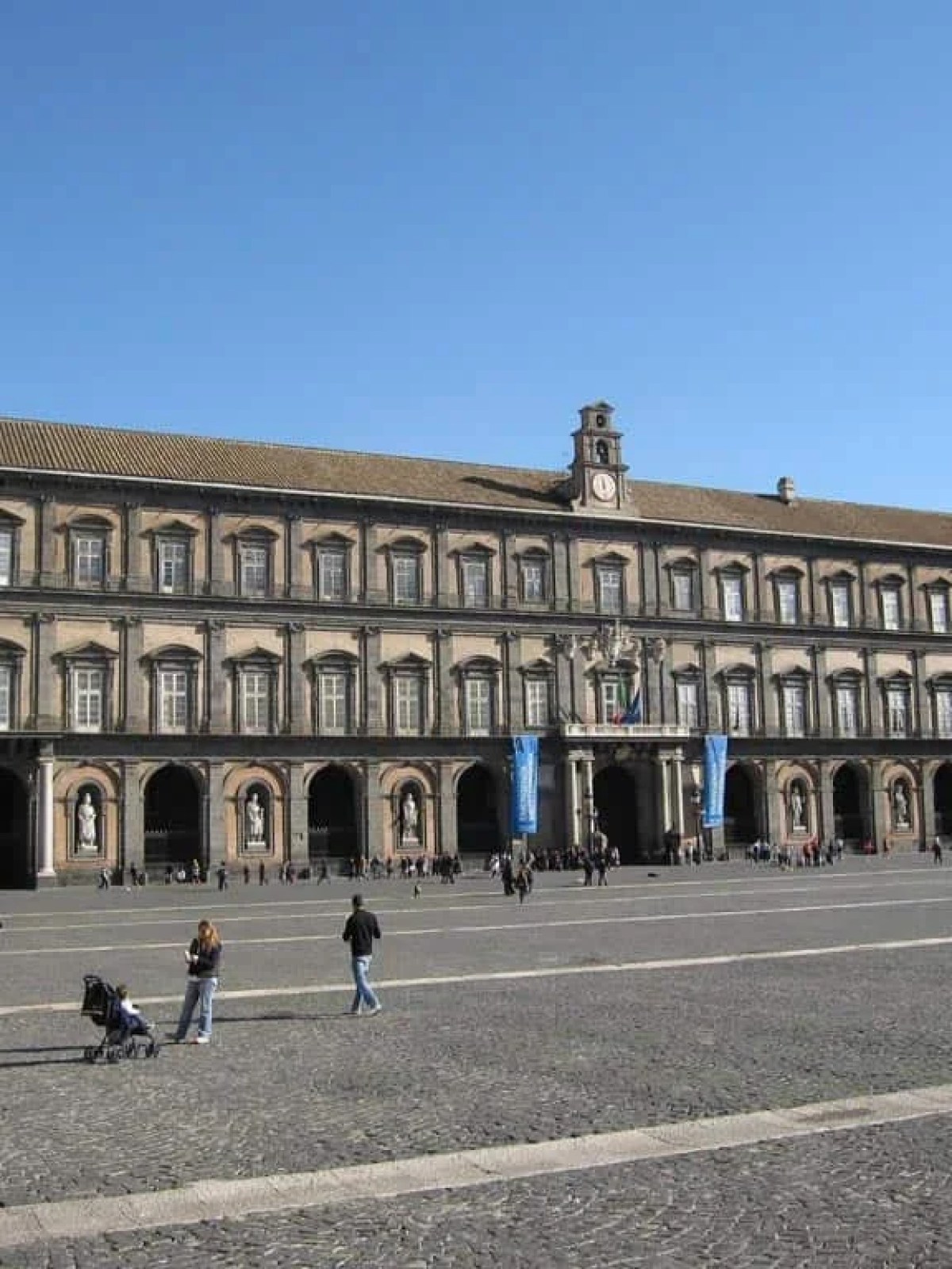 a group of people walking down a street next to Royal Palace of Naples