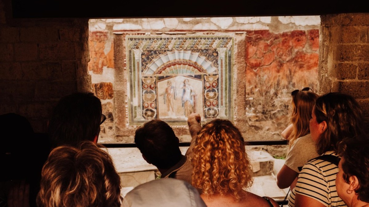 Group of people viewing ancient fresco through a window frame.