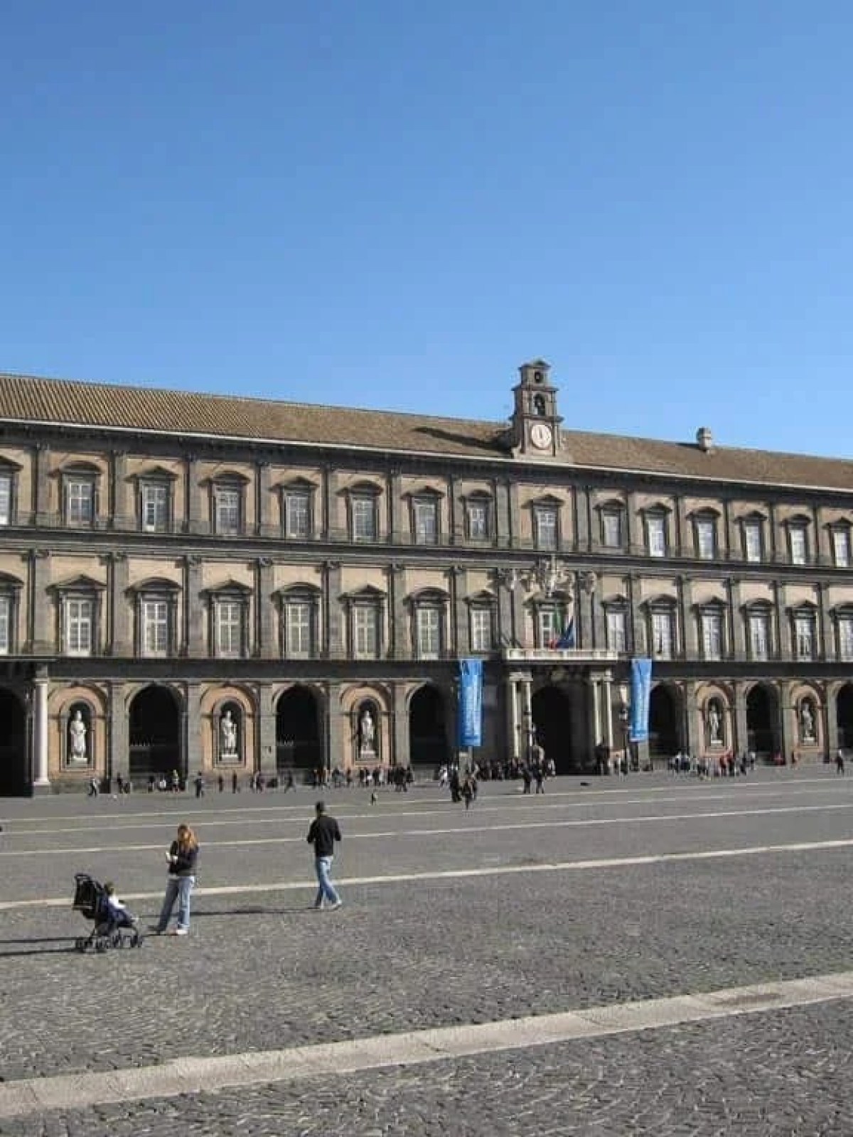a group of people walking down a street next to Royal Palace of Naples