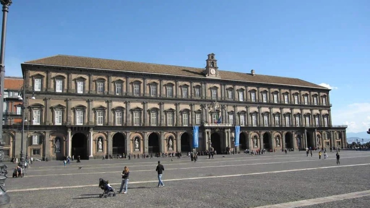 a group of people walking down a street next to Royal Palace of Naples