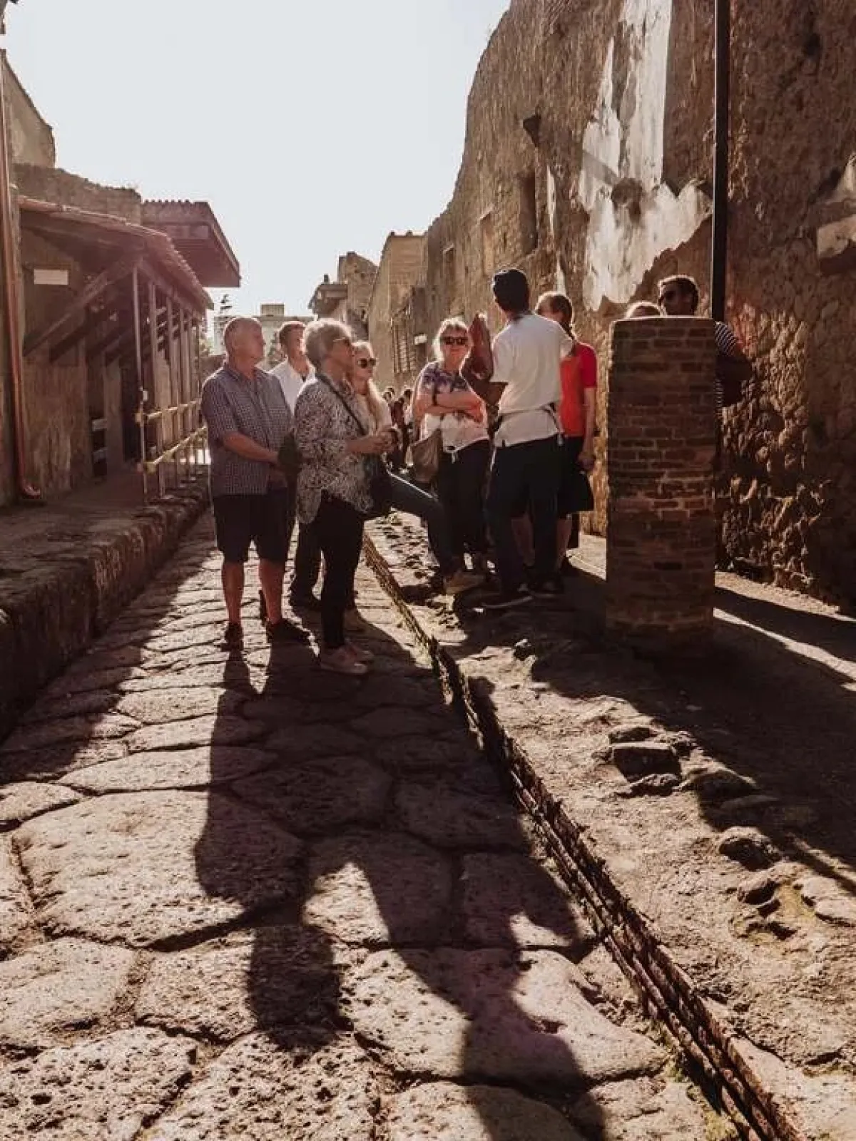 a group of people walking down a sidewalk next to a stone wall