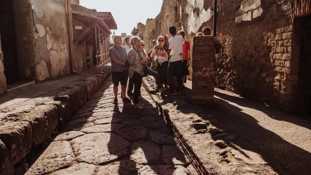 a group of people walking down a sidewalk next to a stone wall