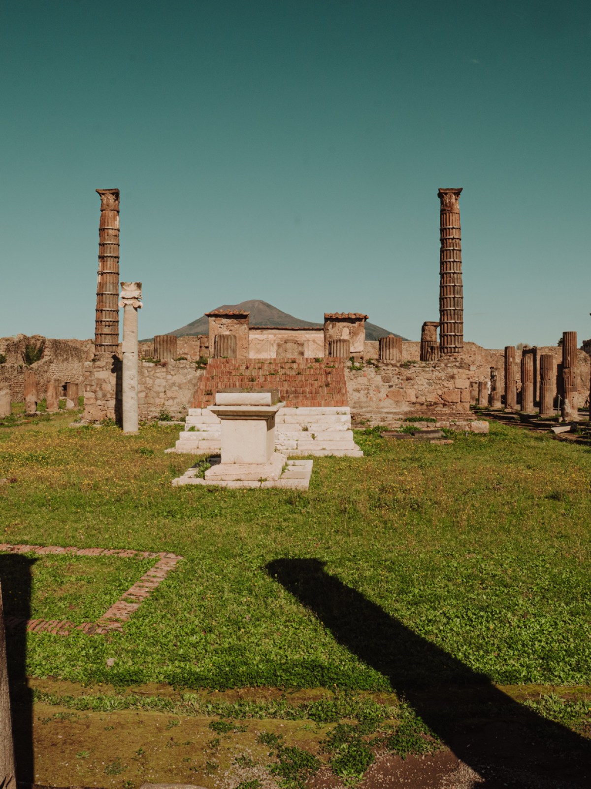 Ancient ruins with columns and a temple, grassy area, and mountain in the background.