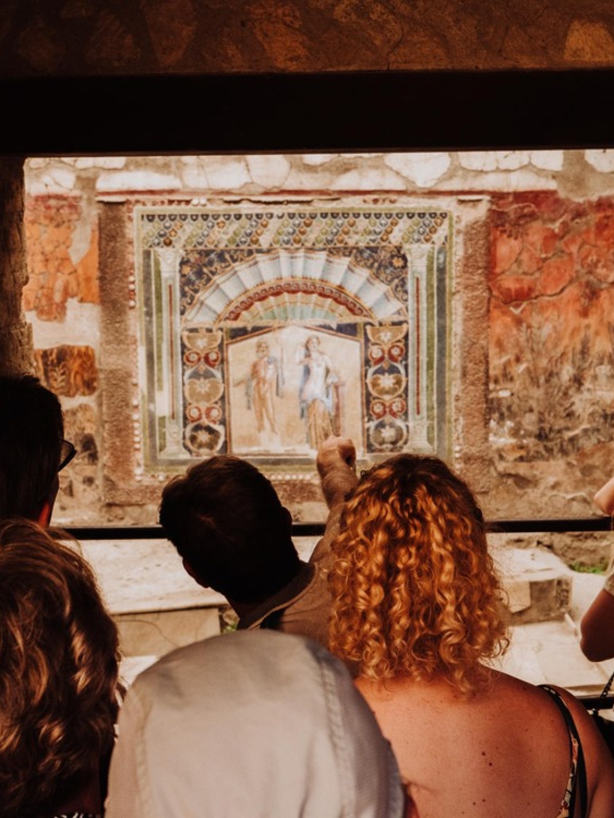 Tourists view an ancient fresco with colorful details in a historic site.