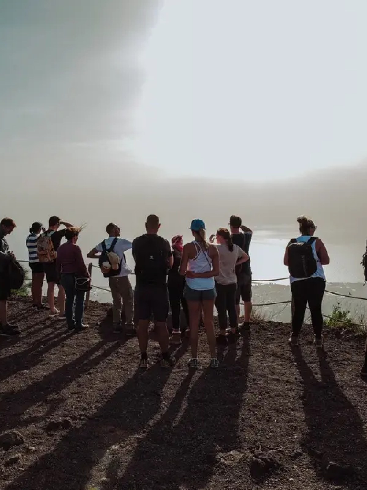 Group of people with backpacks standing on a hilltop, overlooking a bright, hazy horizon.