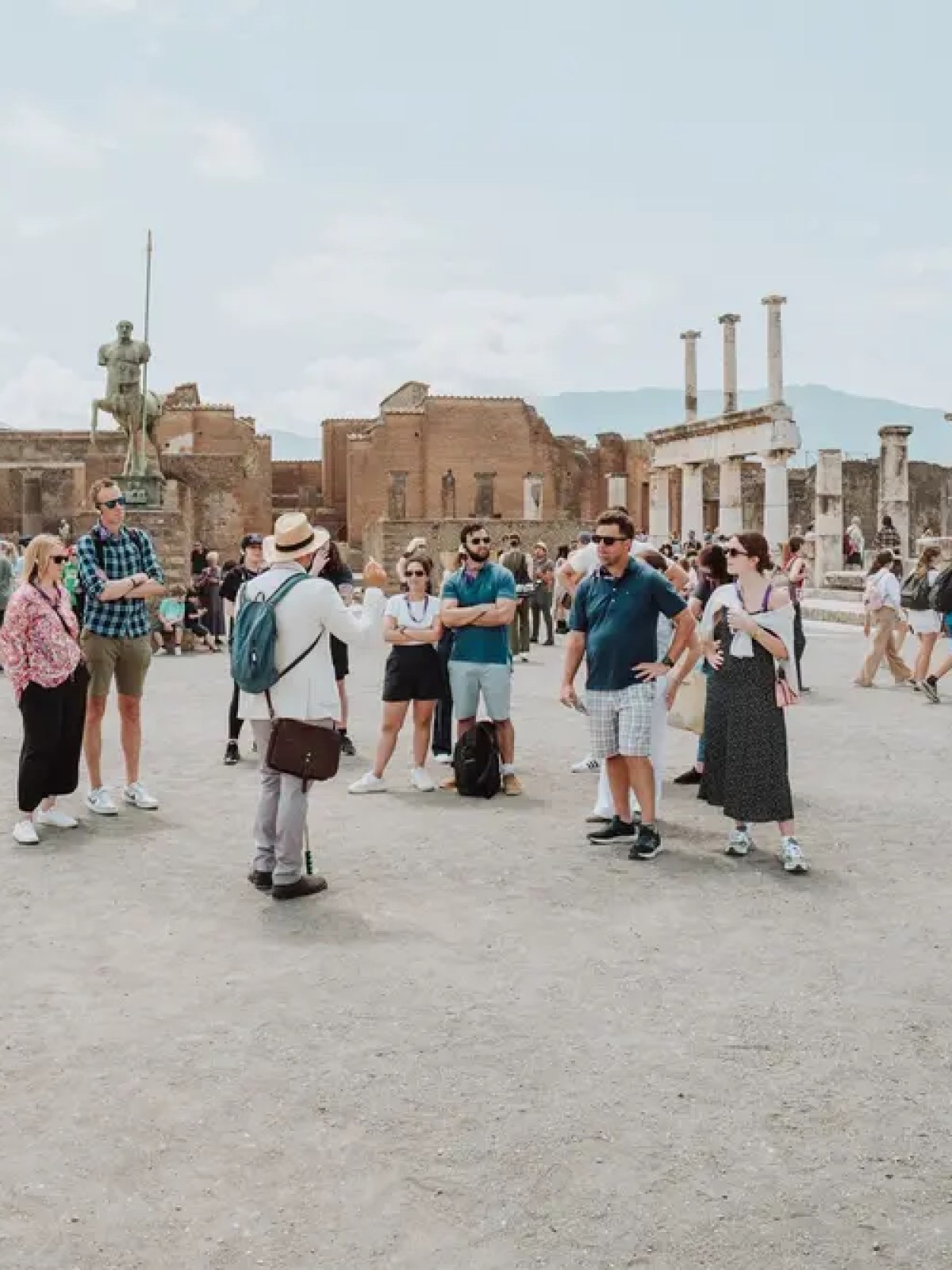 Tourists exploring ancient ruins with columns and a statue in the background.