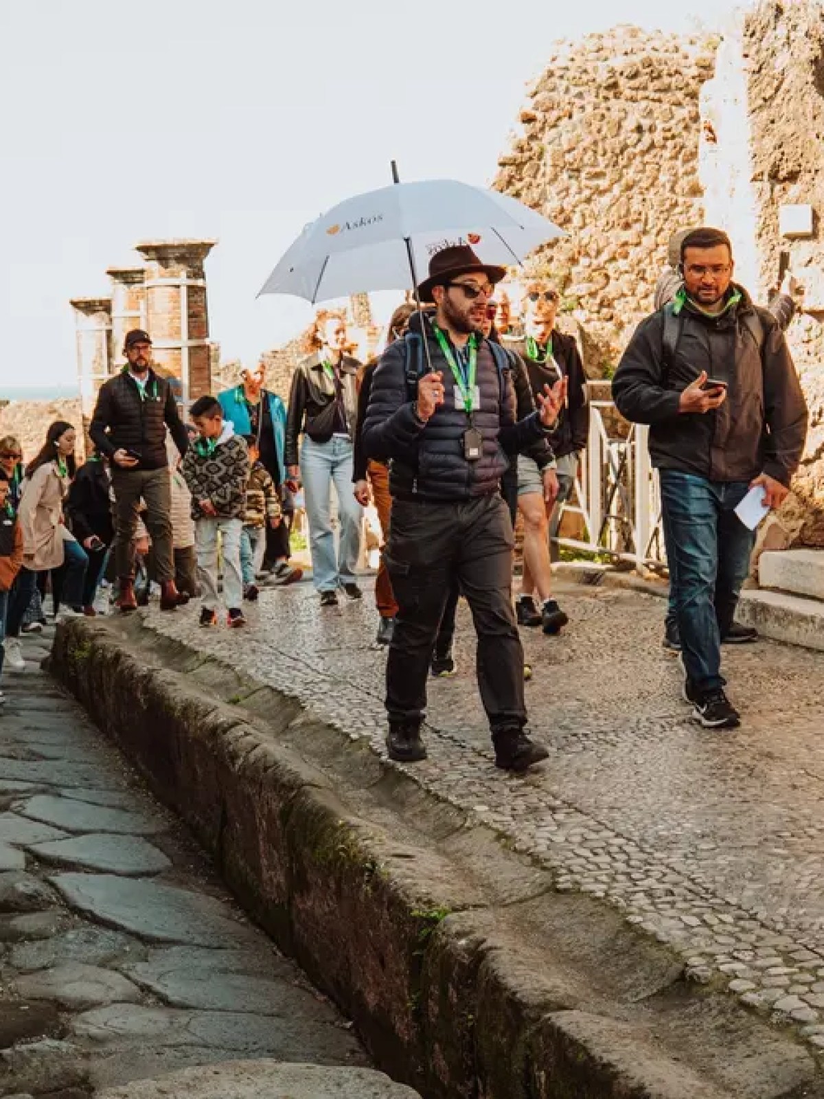 A group of tourists walking through ancient ruins, guided by a person holding an umbrella.