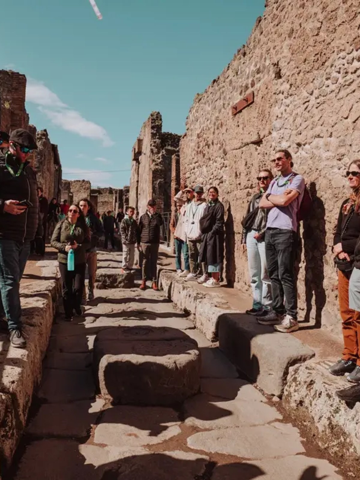 Group of tourists in narrow ancient stone street under clear sky.