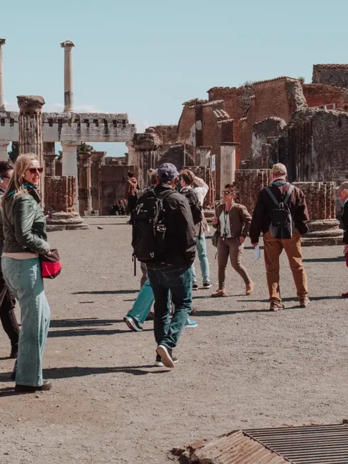Tourists explore ancient ruins with red brick columns and pillars under a clear sky.