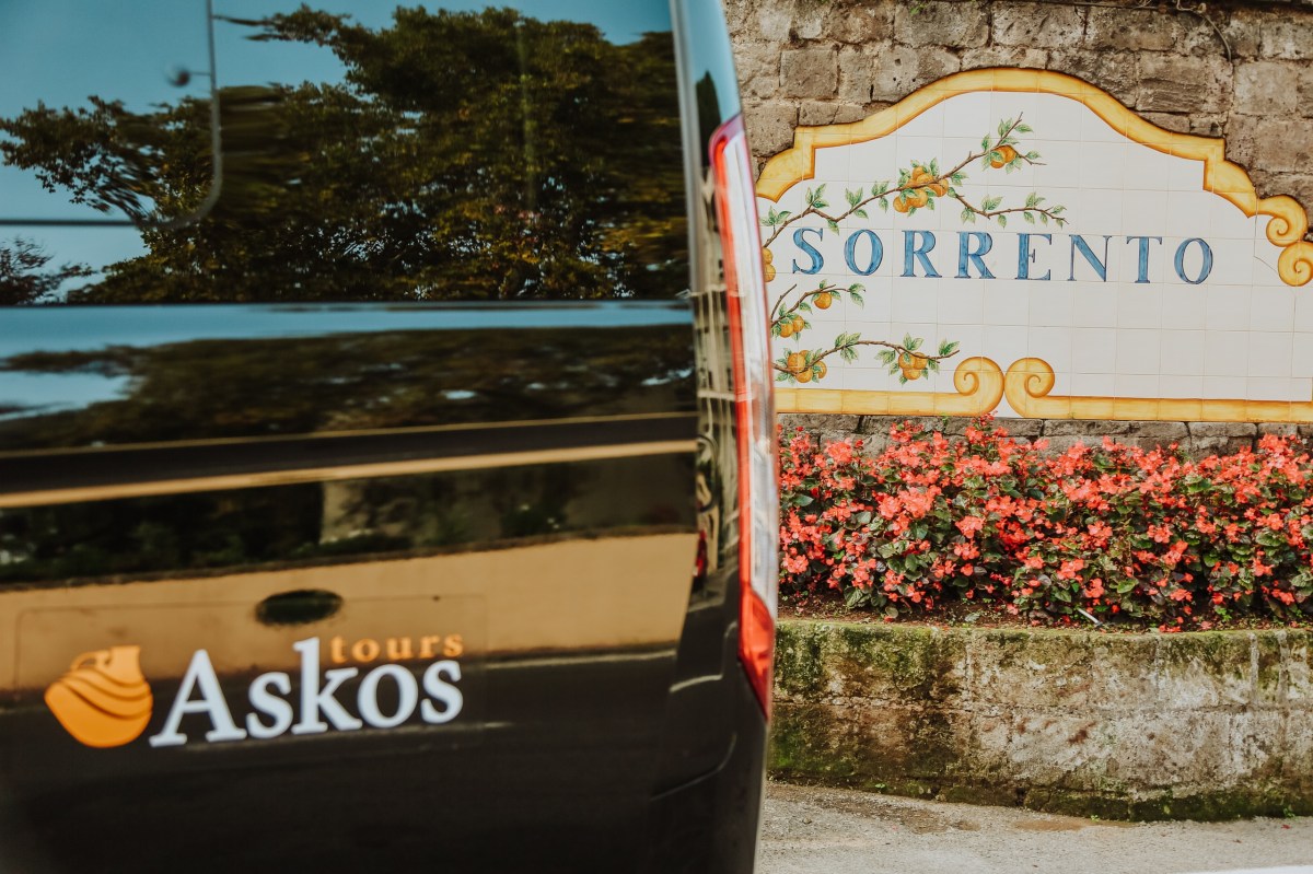 Black van with 'Askos tours' logo near 'SORRENTO' sign with floral design and red flowers.
