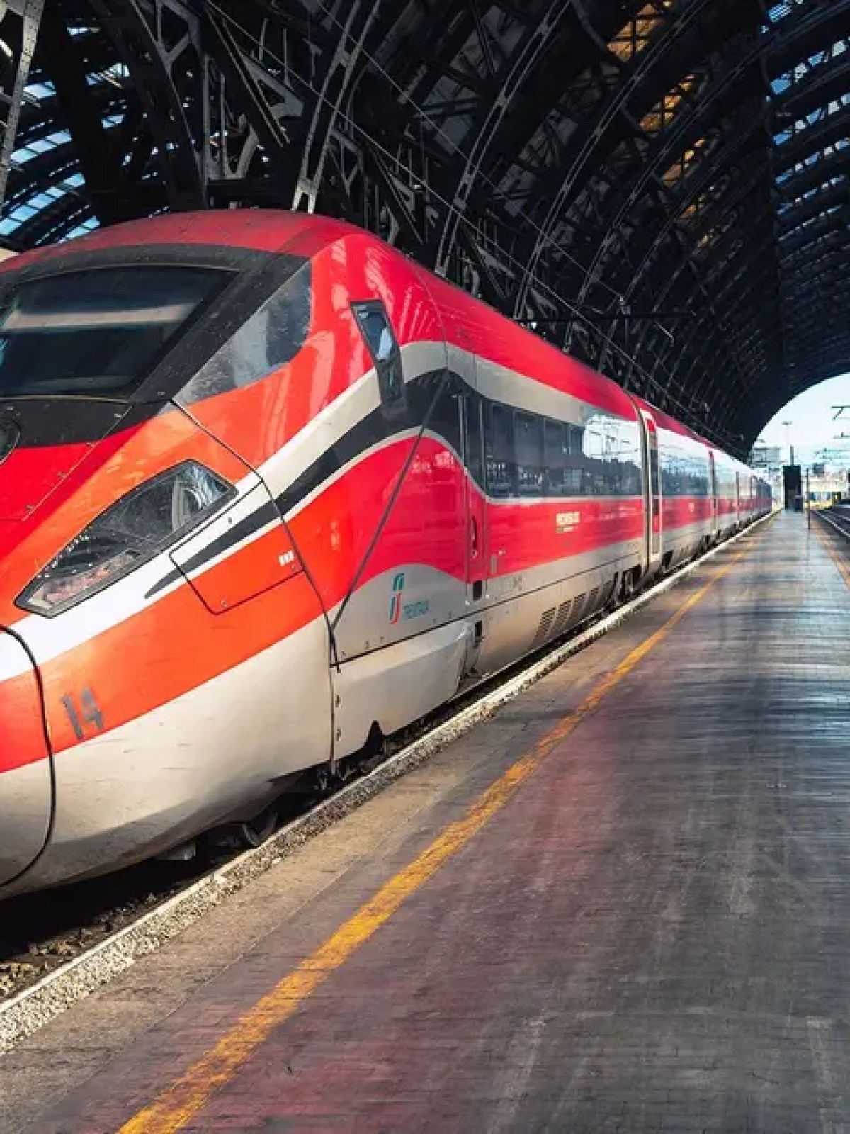 Red high-speed train at a covered station platform, with arched metal roof.