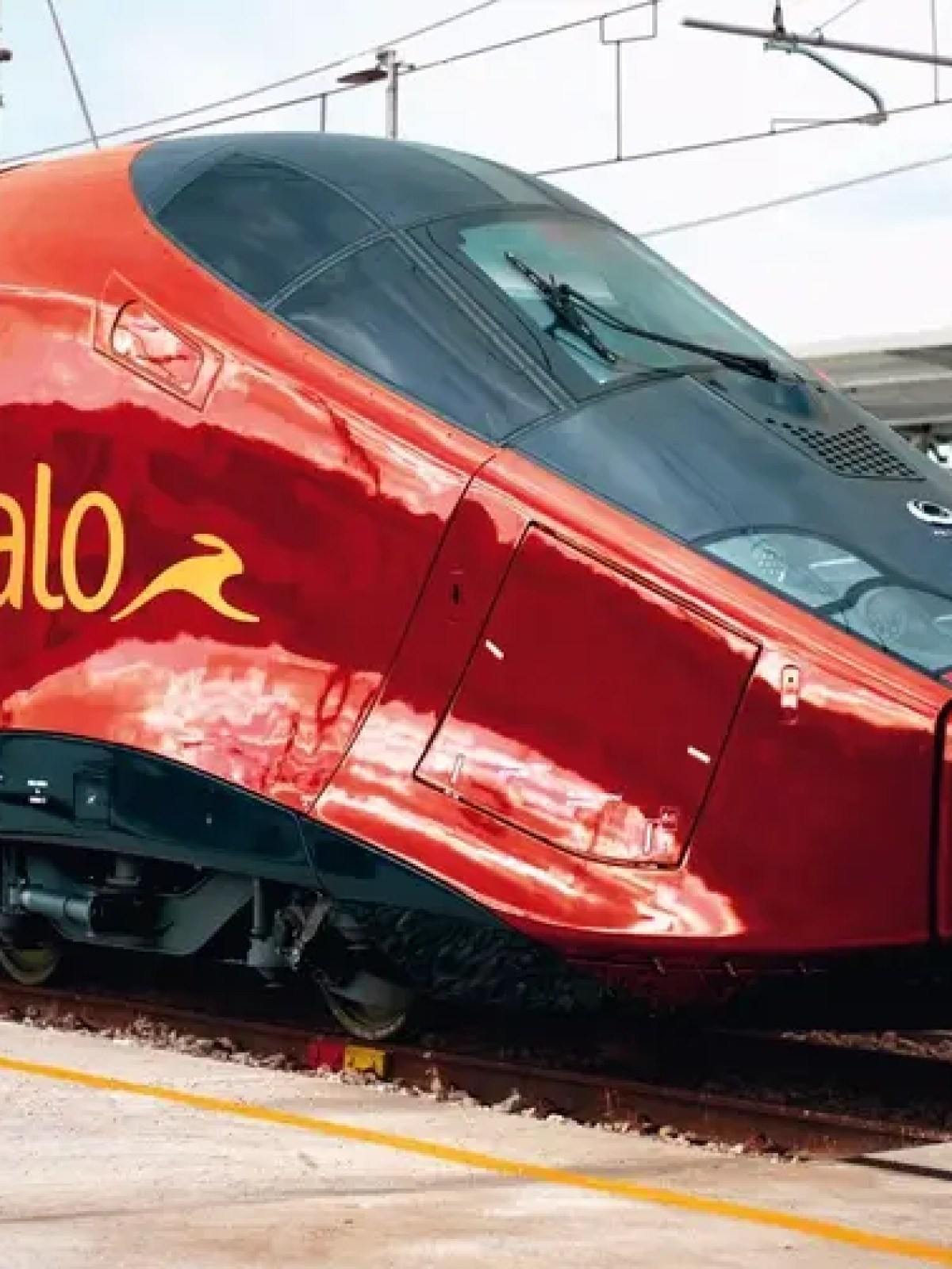 Red high-speed train parked at a station platform on a clear day.