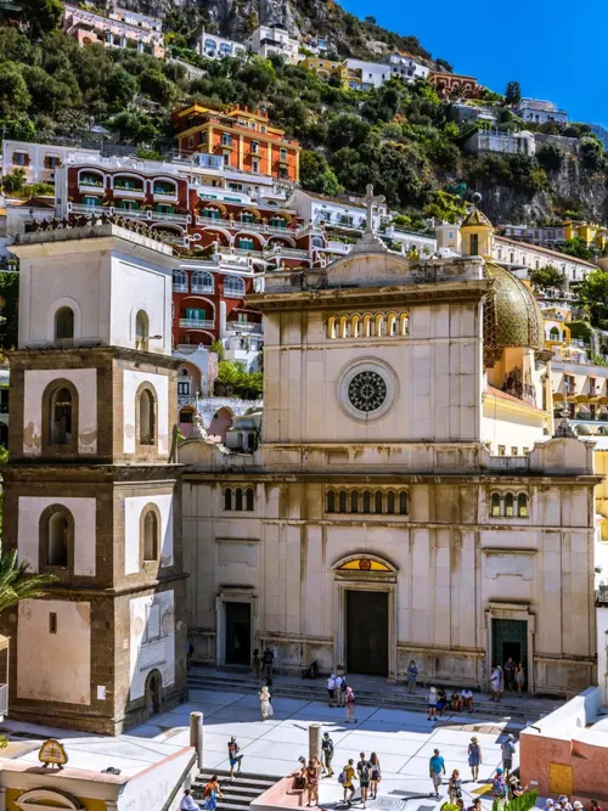 Colorful hillside town with a bell tower and dome against a clear blue sky.