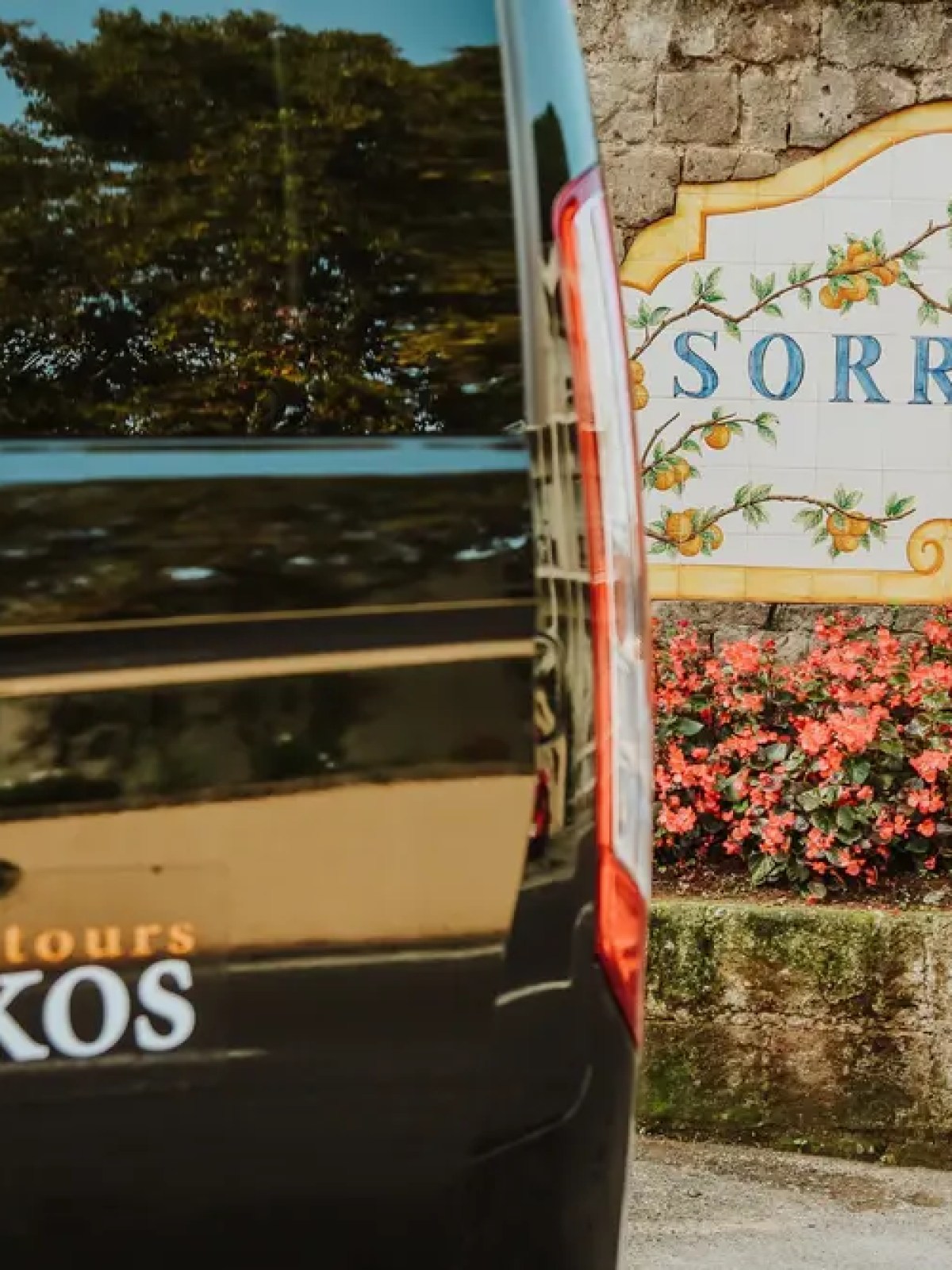 Van with Askos Tours logo near Sorrento sign and red flowers.