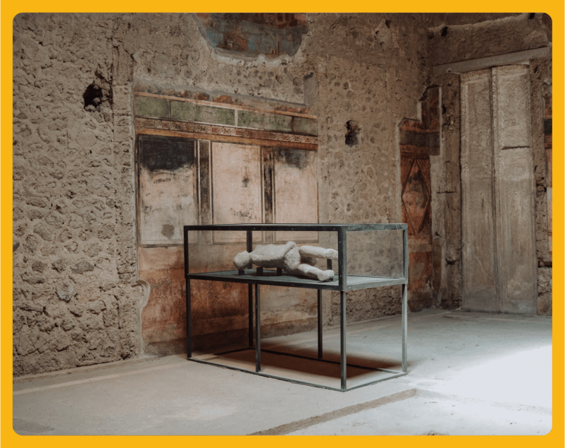Ancient room with frescoes and a clay sculpture in a glass display case.