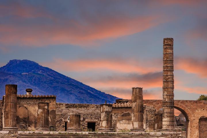 Ancient ruins with columns and mountain under a colorful sunset sky.
